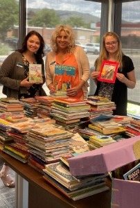 3 people holding books in front of a table covered in books